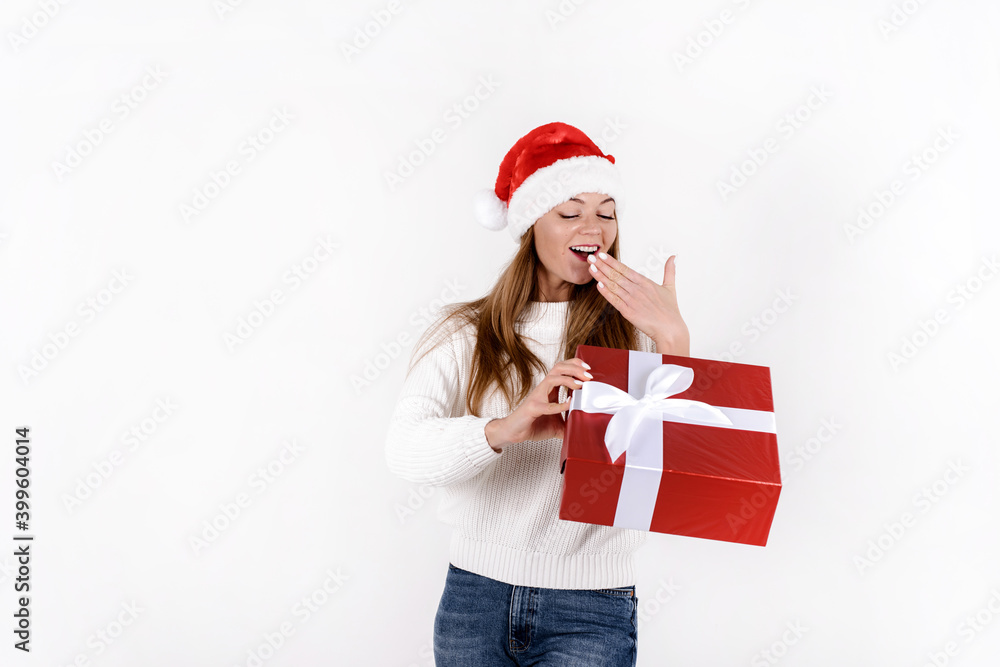 Young cheerful woman holding big gift box and in excitement. Isolated on white background wearing red santa hat