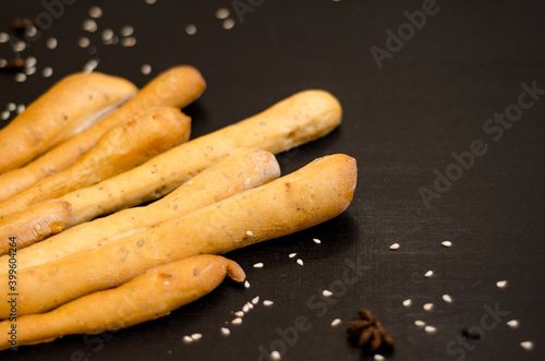 Ruddy grissini, dry long bread with sesame seeds, on black background with spices, star anise and cloves, with copyspace