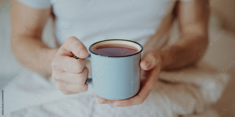 Closeup of man holding cup with tea at a morning in the bed Closeup of man holding cup with tea at a morning in the bed