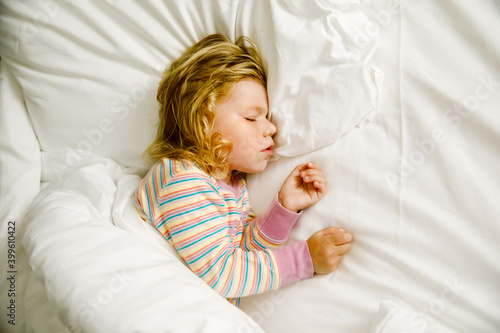 Cute little toddler girl sleeping in big bed of parents. Adorable baby child dreaming in hotel bed on family vacations or at home.