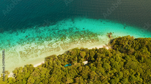 Coastline with forest and palm trees, coral reef with turquoise water, aerial view. Sea water surface in lagoon and coral reef. Seascape of tropical island covered wgreen forest Camiguin, Philippines