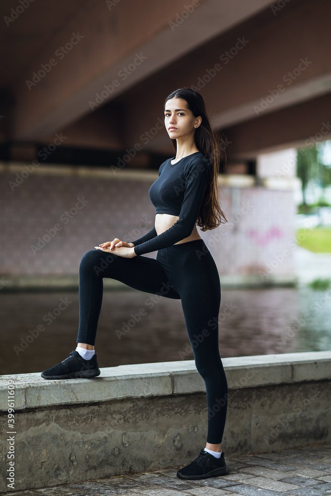 Obraz premium A beautiful brunette in sportswear performs exercises on the waterfront