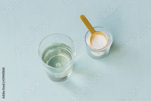 Glass with collagen dissolved in water and collagen protein powder on a light blue table. Healthy lifestyle concept.