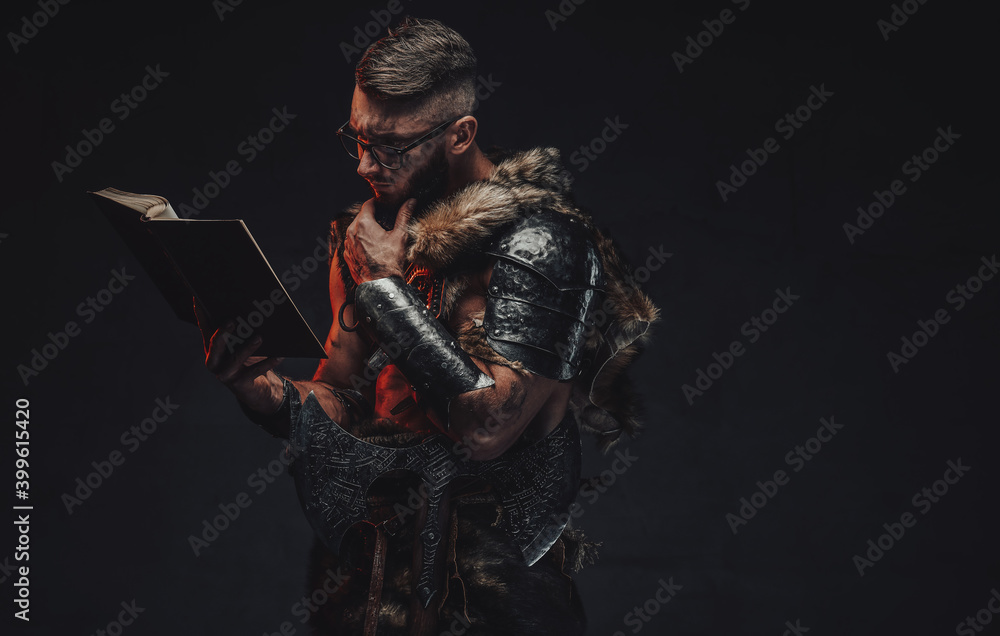 Portrait of clever scandinavian warrior with eyeglasses reading a book with arm under his chin in dark background.