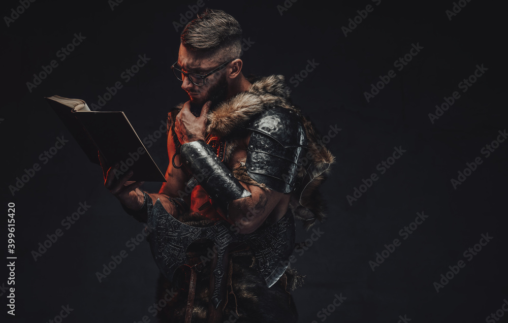 Portrait of clever scandinavian warrior with eyeglasses reading a book with arm under his chin in dark background. Portrait of clever scandinavian warrior with eyeglasses reading a book with arm under his chin in dark background.