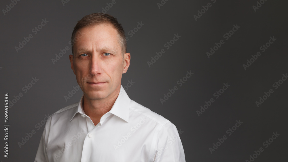 Clean-shaven middle-aged man in white shirt stands against a dark background - obrazy, fototapety, plakaty 