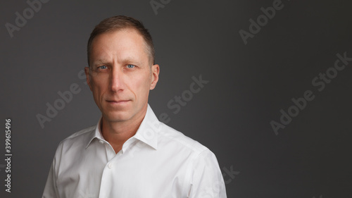 Clean-shaven middle-aged man in white shirt stands against a dark background