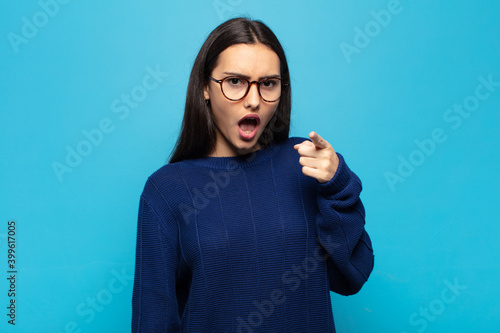 young hispanic woman pointing at camera with an angry aggressive expression looking like a furious, crazy boss photo