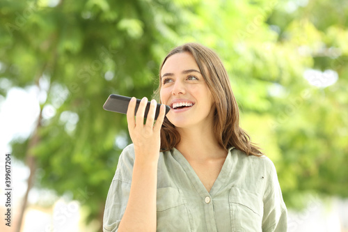 Happy woman recording audio message on phone in a park