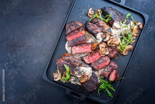 Modern style barbecue dry aged wagyu Brazilian picanha steaks from the sirloin cap of rump beef sliced and served cream sauce and mushrooms as top view on a design tray with copy space left