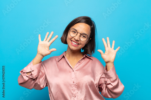 young hispanic woman smiling and looking friendly, showing number ten or tenth with hand forward, counting down photo