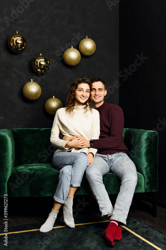 guy hugs a girl while sitting on the couch in Christmas clothes. the wall is decorated with garlands and Christmas decor. new year holidays.