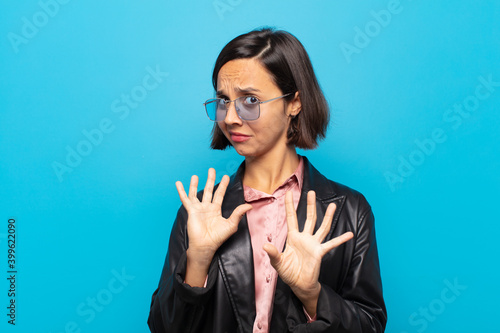 young hispanic woman feeling disgusted and nauseous, backing away from something nasty, smelly or stinky, saying yuck