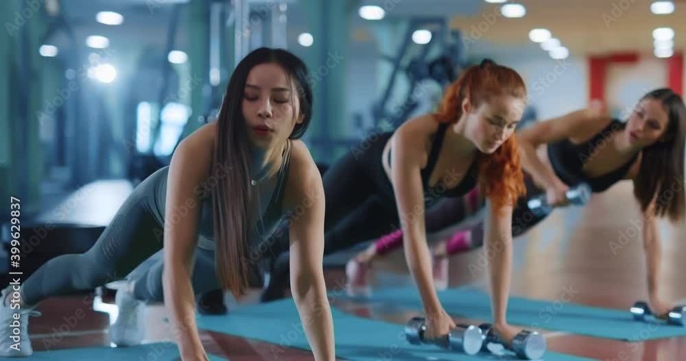 Multi-cultural women doing push up exercise with dumbbells training out together enjoying xompany in the gym. Strong females. Girl power. Multi-ethnic. Multi-cultural women doing push up exercise with dumbbells training out together enjoying xompany in the gym. Strong females. Girl power. Multi-ethnic.