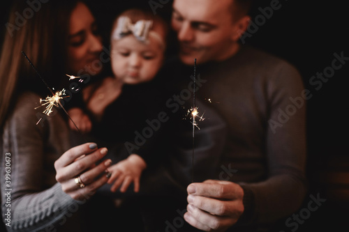 portrait of happy family, mom, dad and baby girl with sparklers and light. family in anticipation of Christmas. selective photo.
