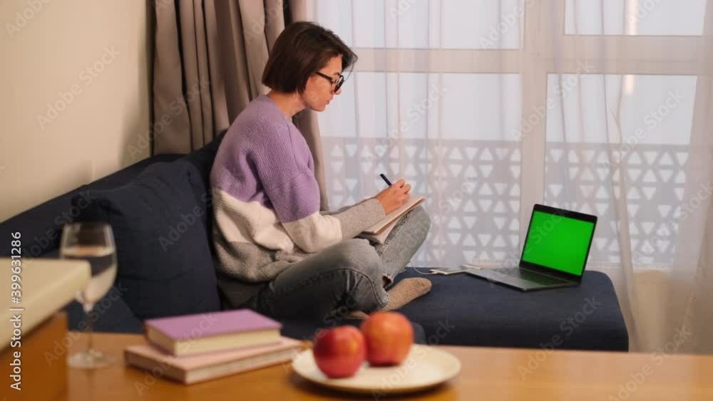Woman studies at home works writes something in a notebook, looks at a laptop Woman studies at home works writes something in a notebook, looks at a laptop