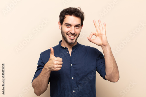 young handsome man feeling happy, amazed, satisfied and surprised, showing okay and thumbs up gestures, smiling