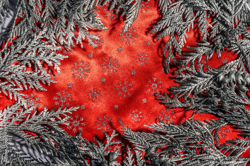 Christmas frame composition with silver thuja branches against red background. Overhead view, flat lay with copy space