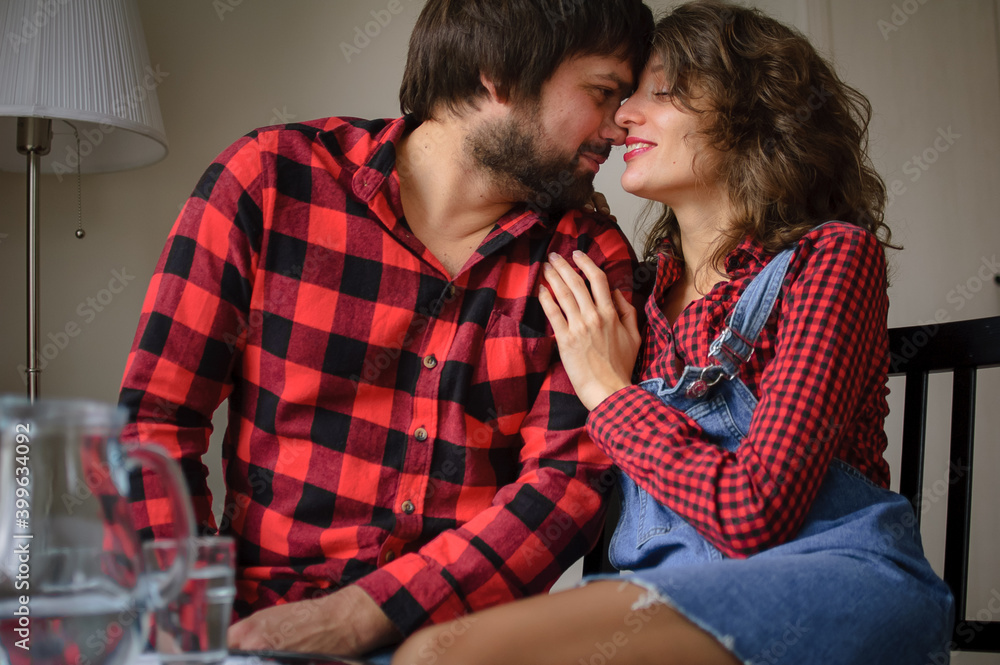 Beautiful brunette girl and handsome bearded guy in similar checkered red shirts look at each other and smile during celebration St. Valentine Day Beautiful brunette girl and handsome bearded guy in similar checkered red shirts look at each other and smile during celebration St. Valentine Day
