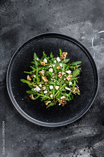salad with arugula, nuts, feta cheese, olive oil, herbs. Black background. Top view
