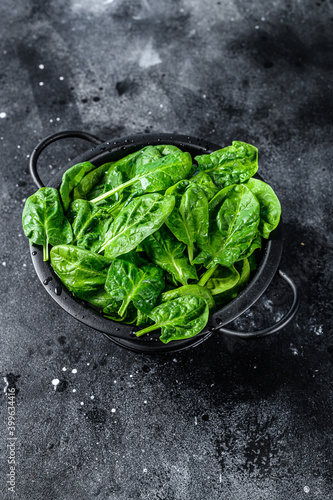 Young raw spinach in a colander. Black background. Top view