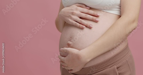 Wallpaper Mural Close up shot of young pregnant woman stroking her big belly, pink studio background, empty space Torontodigital.ca
