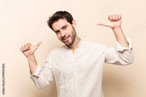 young handsome man feeling proud, arrogant and confident, looking satisfied and successful, pointing to self