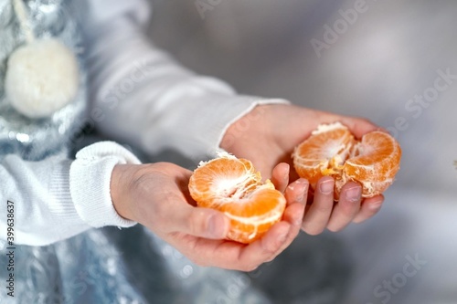 a woman's hands in a shiny suit hold a peeled tangerine