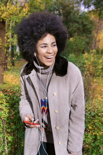 an african american girl listening to music with headphones in the park © Aydan