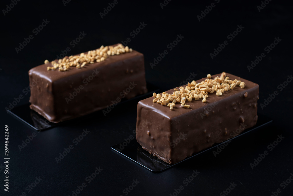 Two mousse desserts with hazelnut praline, milk chocolate and covered gourmet chocolate-nut glaze on a black background close-up. Two mousse desserts with hazelnut praline, milk chocolate and covered gourmet chocolate-nut glaze on a black background close-up.