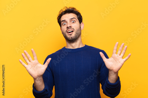 young handsome man feeling stupefied and scared, fearing something frightening, with hands open up front saying stay away photo