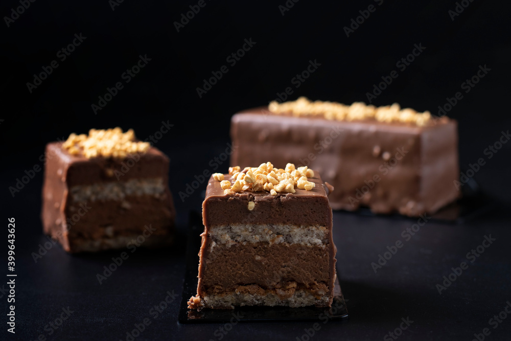 Sliced mousse desserts with hazelnut praline, milk chocolate and covered gourmet chocolate-nut glaze on a black background. Close-up. Sliced mousse desserts with hazelnut praline, milk chocolate and covered gourmet chocolate-nut glaze on a black background. Close-up.