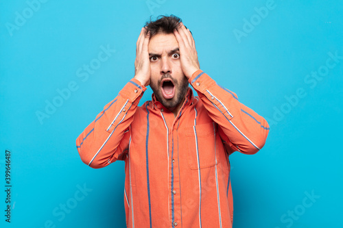 young handsome man looking unpleasantly shocked, scared or worried, mouth wide open and covering both ears with hands photo