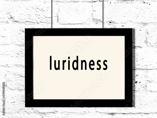 Black frame hanging on white brick wall with inscription luridness