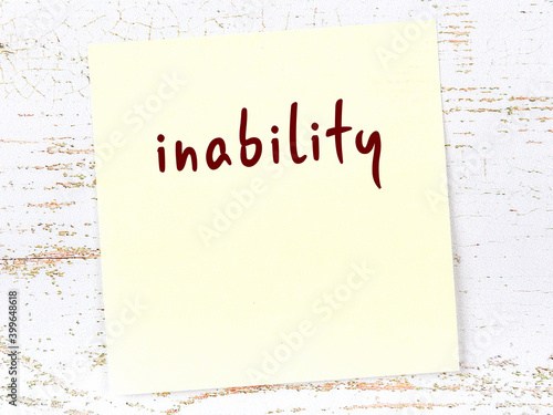 фотографія Yellow sticky note on wooden wall with handwritten word inability