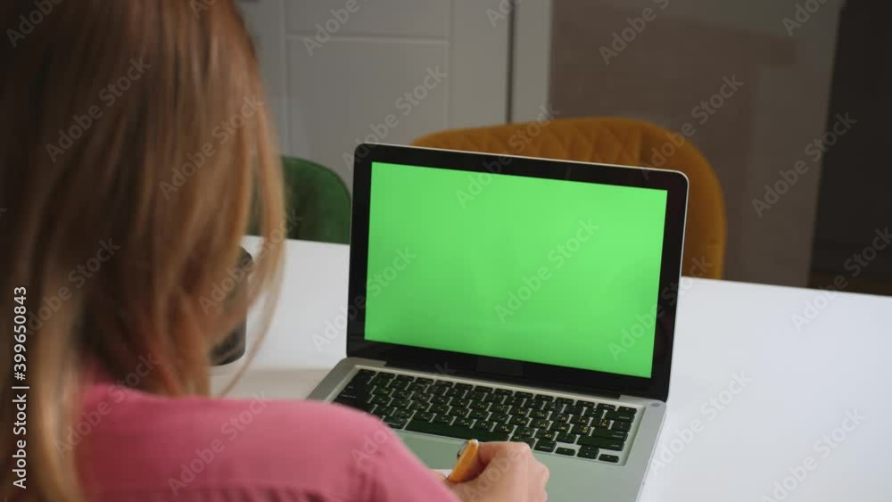 Green screen laptop computer concept: online distance education, video call conference. Over the shoulder woman student at home study writes information in a notebook. Green screen laptop computer concept: online distance education, video call conference. Over the shoulder woman student at home study writes information in a notebook.