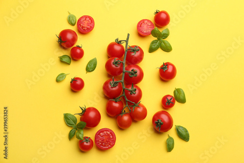 Fresh cherry tomatoes and basil leaves on yellow background, flat lay