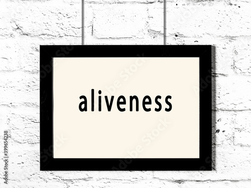 Black frame hanging on white brick wall with inscription aliveness photo