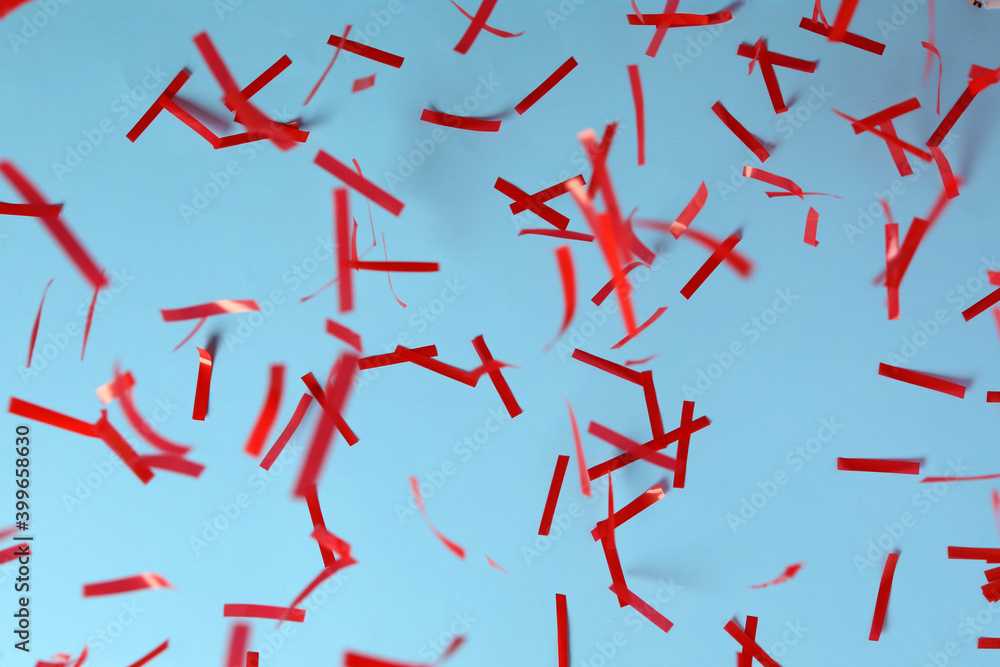Shiny red confetti falling down on light blue background