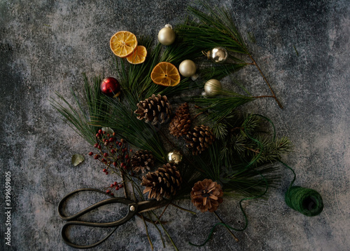 Arrangement of Christmas decorations: green conifer, red berries, ribbons and oranges on a dark background. 