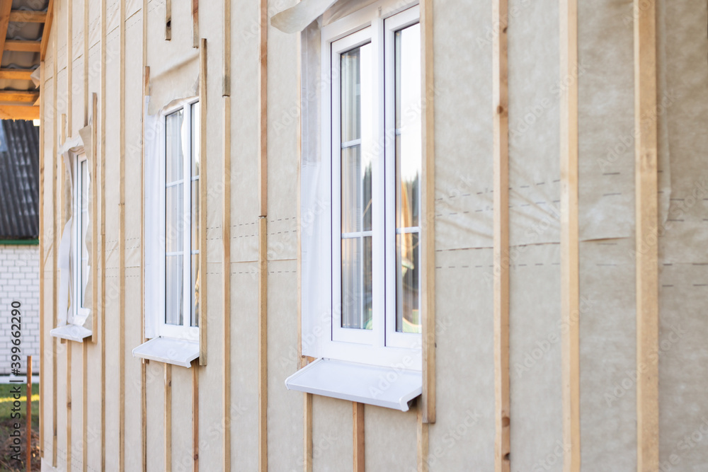 Wall, pediment of a house under construction with windows, vertical beams and a protective membrane for wall cladding Wall, pediment of a house under construction with windows, vertical beams and a protective membrane for wall cladding