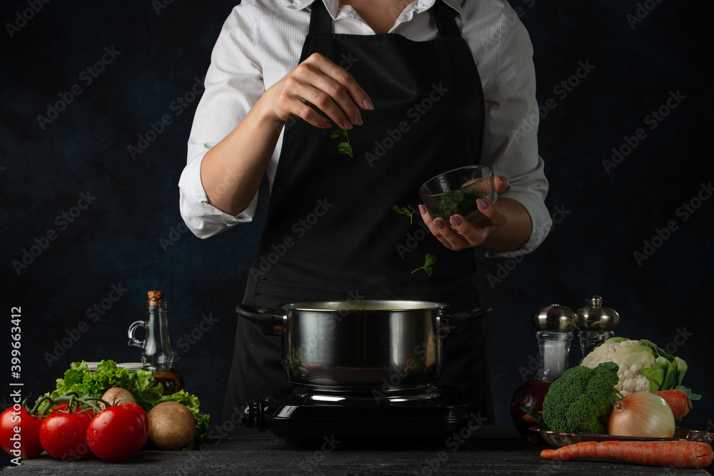Professional chef pours parsley into pan for cooking soup on dark blue background. Backstage of preparing meal. Healthy dish. Food concept. Frozen motion. Cookbook. Professional chef pours parsley into pan for cooking soup on dark blue background. Backstage of preparing meal. Healthy dish. Food concept. Frozen motion. Cookbook.