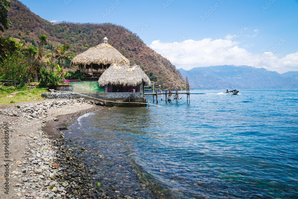 Jetty hut with straw roof at the coast of lake Atitlan with passing by speed boat at Santa Cruz La Laguna, Guatemala Jetty hut with straw roof at the coast of lake Atitlan with passing by speed boat at Santa Cruz La Laguna, Guatemala