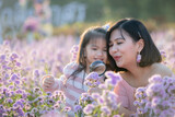 Cute asian child girl and her mother enjoying with beautiful flower together and little girl holding magnifier looking on flower with fun and curiously in the flower garden.