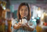 Asian woman holding delicious ice cream dessert in a cup in night market. Thai famous gourmet street dessert food. Street food in Thailand.