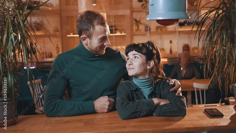 Caucasian beautiful young couple staying in cafe hugging together looking at camera smiling. Young family. Relationships. Dating. Cafeteria interior. Portrait. Caucasian beautiful young couple staying in cafe hugging together looking at camera smiling. Young family. Relationships. Dating. Cafeteria interior. Portrait.