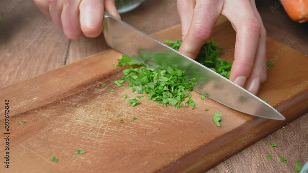 Close-up of chopping parsley with a chef knife on a cutting board in 4K. Concept of a female hand cutting greens in slow-motion.