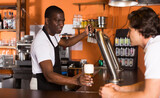 Young man bartender giving beer with foam to man client in bar..