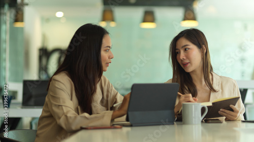 Two female office workers talking to each other while working in meeting room