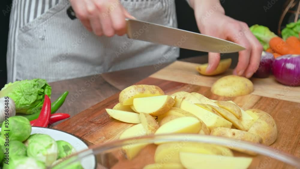 A close-up look of slicing fresh potatoes on a wooden cutting board in 4k. Concept of chopping fresh potatoes as a vegetable for roast chicken along with other vegetables on the table. A close-up look of slicing fresh potatoes on a wooden cutting board in 4k. Concept of chopping fresh potatoes as a vegetable for roast chicken along with other vegetables on the table.